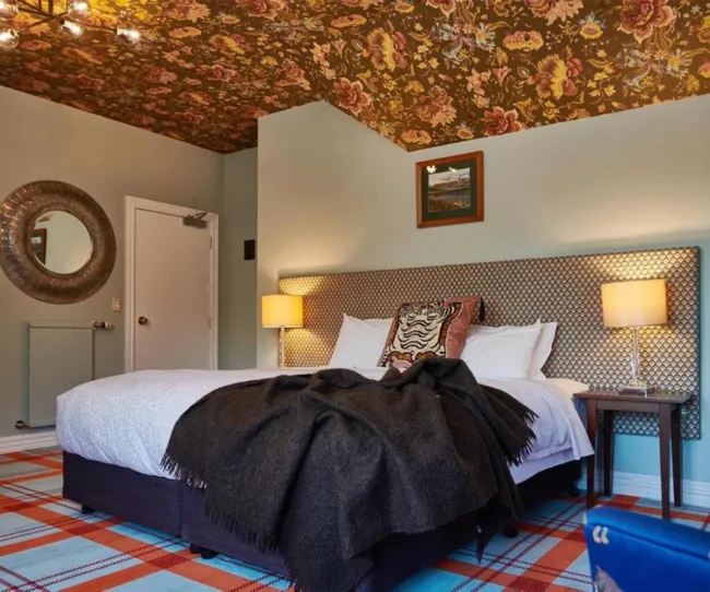 Chambre confortable avec plafond floral, tapis à carreaux, grand lit, oreillers décoratifs, lampes sur les tables latérales et art au-dessus de la tête de lit.