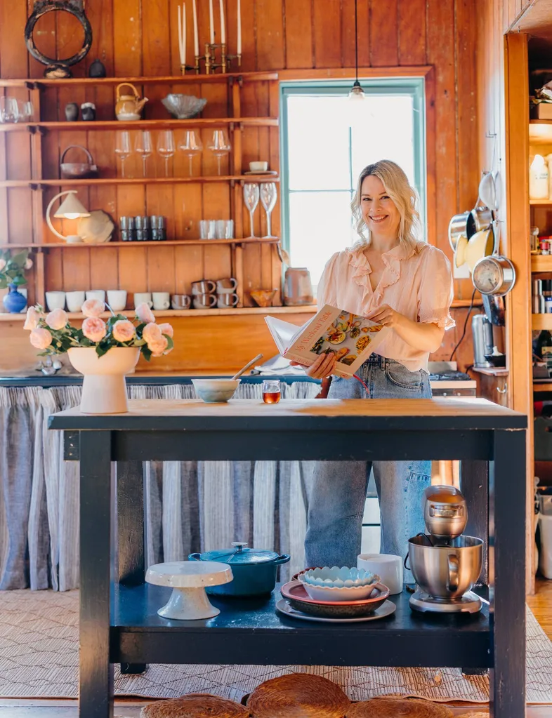 Gretchen Lowe debout dans la cuisine avec livre de cuisine et fleurs