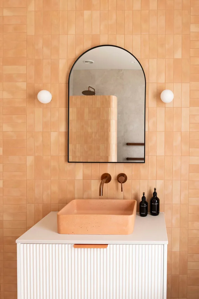 Tiles de couleur pêche dans une salle de bain avec un miroir ovale et un lavabo blanc