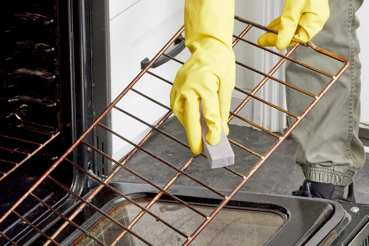 DIYer using a pumice stone to remove baked on gunk from oven grates.