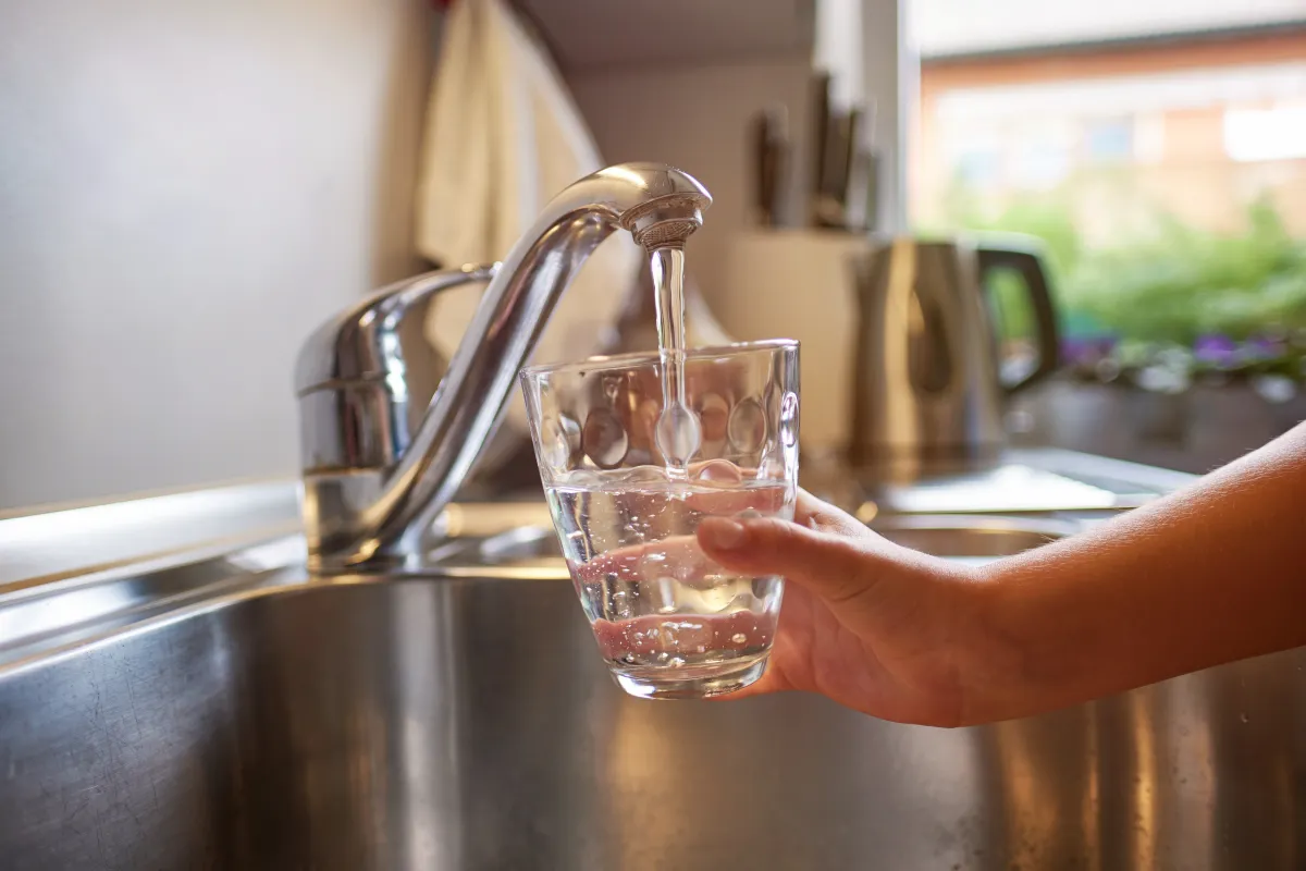 Small hand holds a glass under a kitchen tap to catch water.