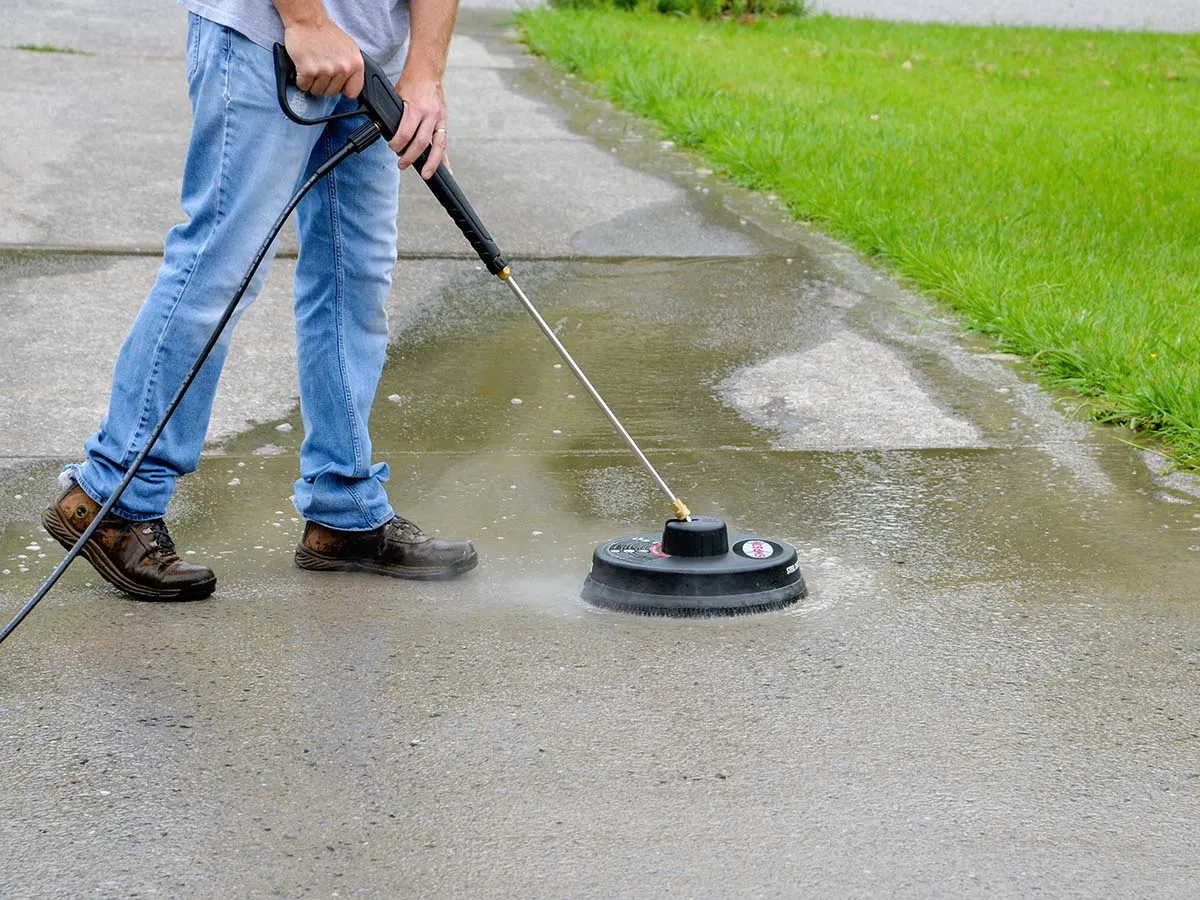 Man washing a driveway with a pressure washer surface cleaner.