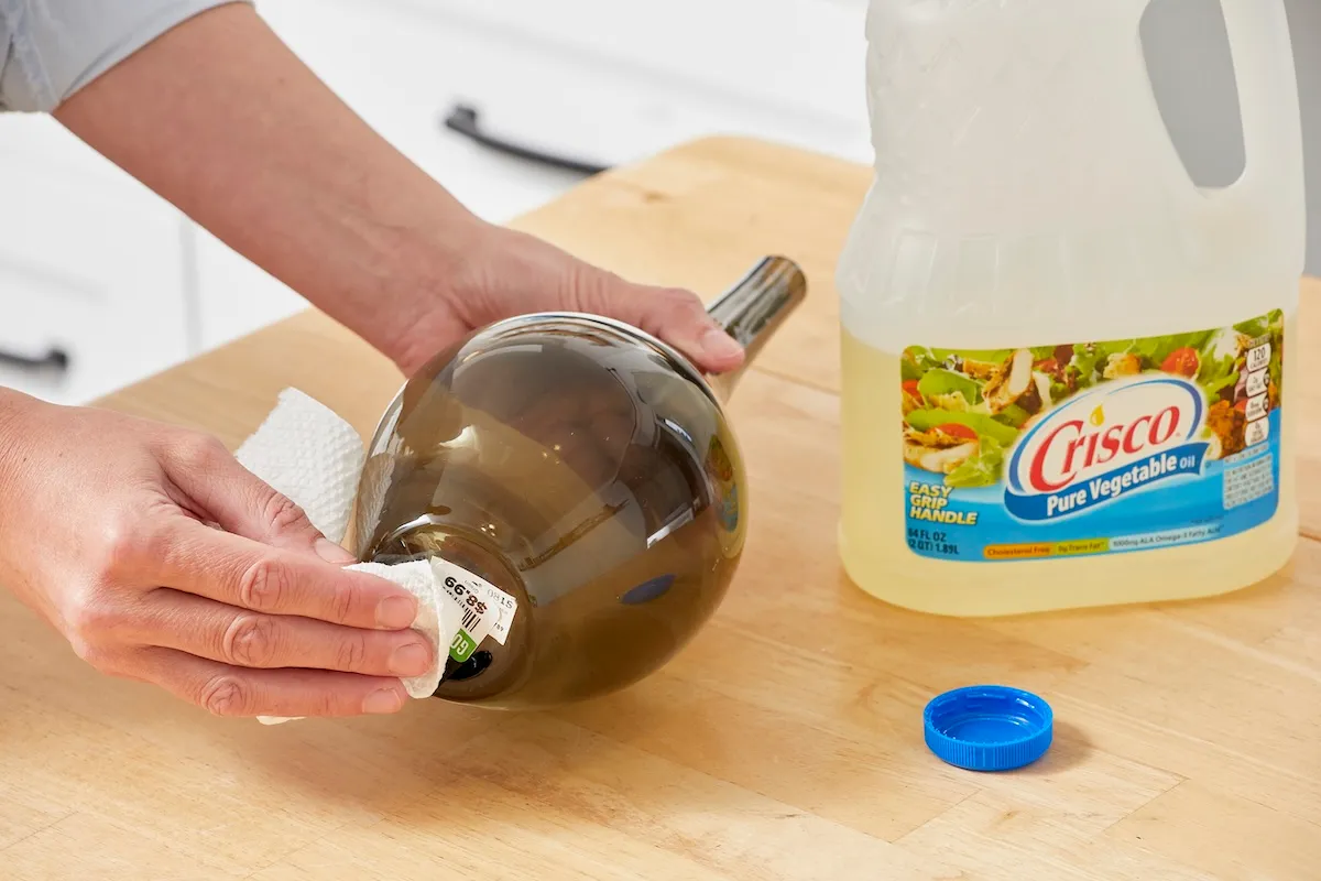 Woman applies cooking oil to a sticker on the bottom of a vase.