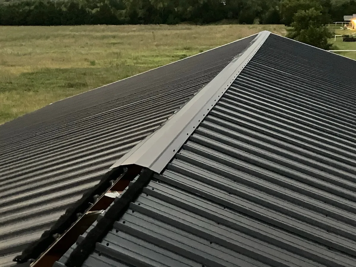 Partially installed ridge venting on a black metal roof.