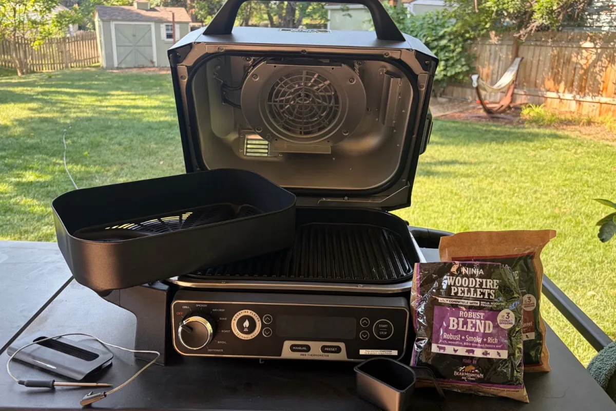 The Ninja OG751 Woodfire Pro outdoor grill on a table outside with its inlcluded smoker pellets and thermometer probe