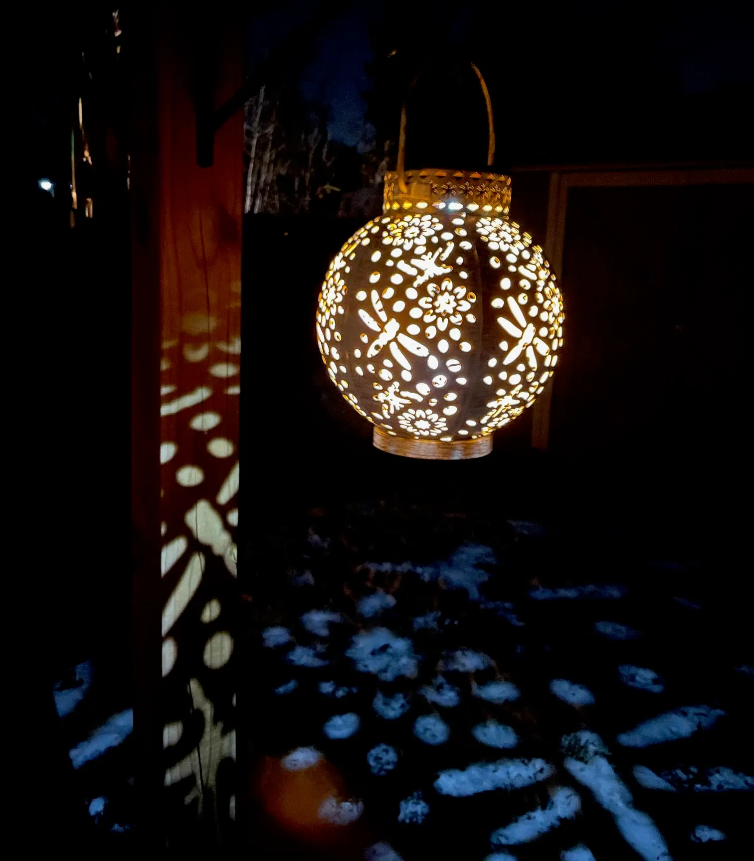 Kooper Solar-Powered Integrated LED Outdoor Lantern hanging from a hook on a deck post lit up at night