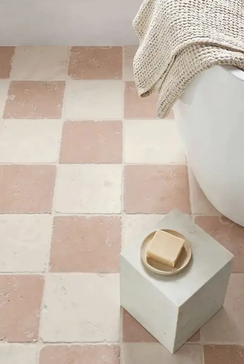 Bianco and Rosa Perlino tumbled marble checkerboard tile next to a small white table and white bathtub.