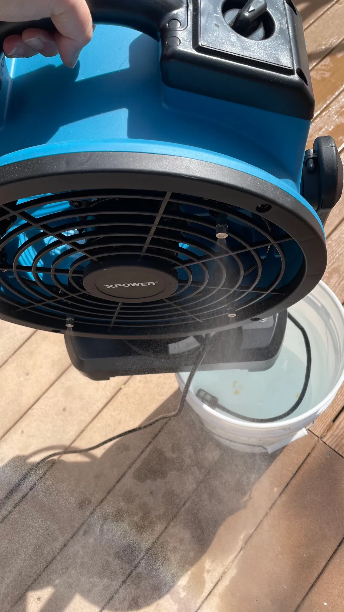 A person holding the XPower FM-88W misting fan by its handle to show the water pump in a bucket of water