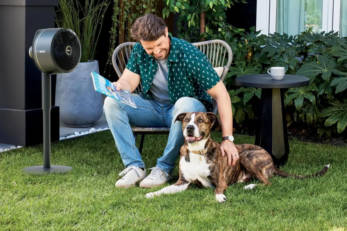 Un homme et un chien dans une cour près du Shark FlexBreeze Fan With InstaCool