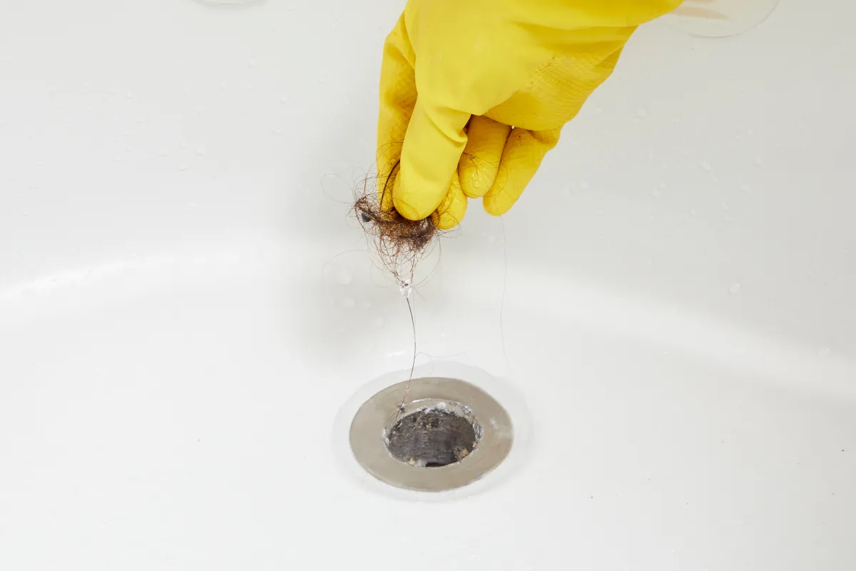 A person pulling a clog out of a shower drain.