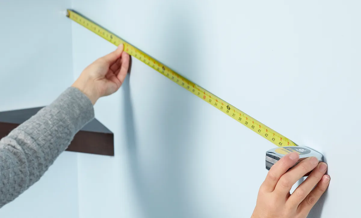 Woman uses a measuring tape to measure wall from corner.