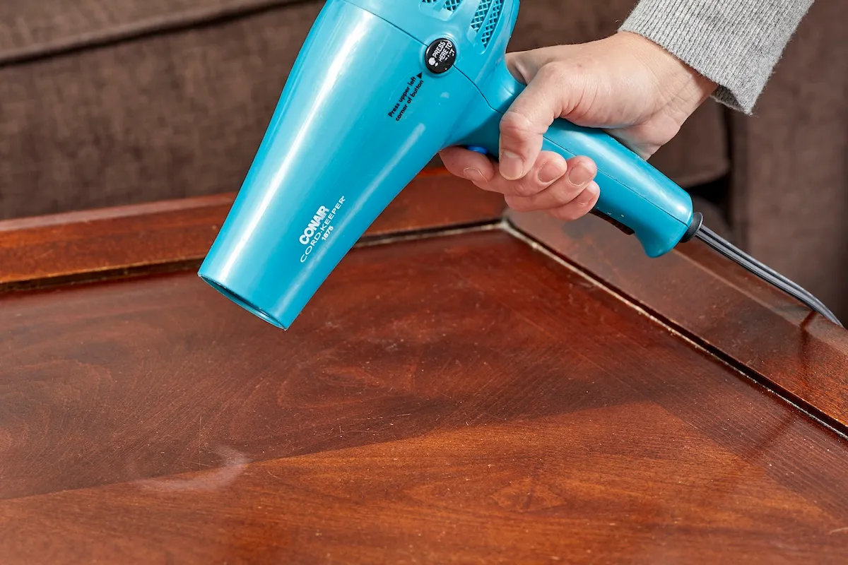 A person using a hair dryer to remove water stains from wood.