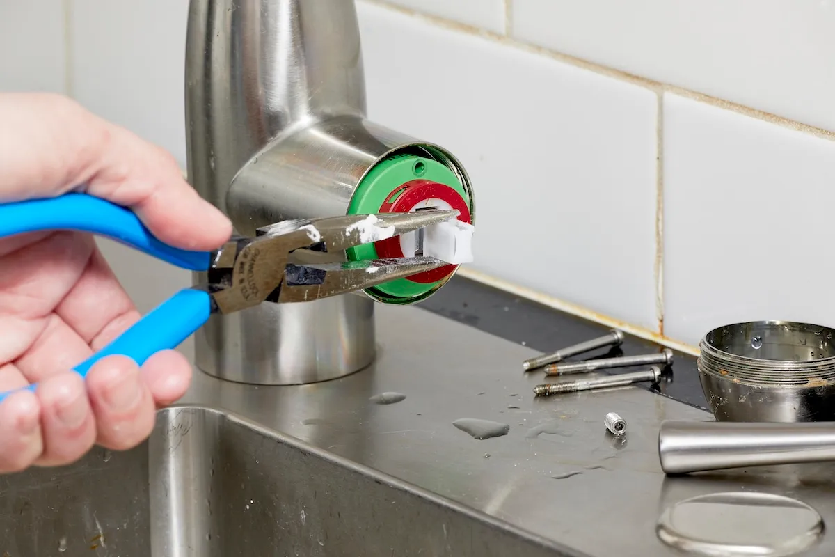Person uses needle-nose pliers to remove faucet cartridge from kitchen faucet.