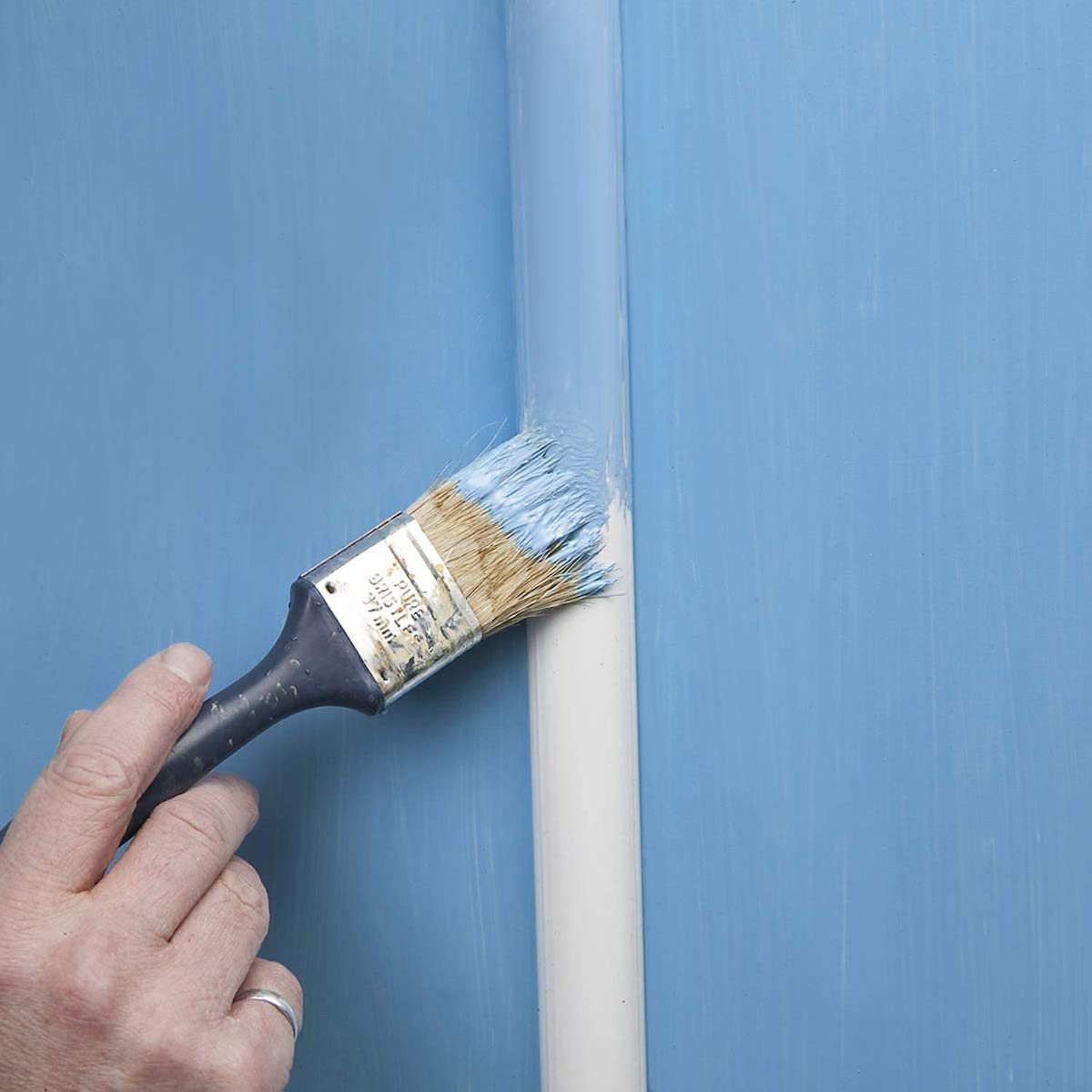 Person painting a cord cover on a blue wall the same color blue.