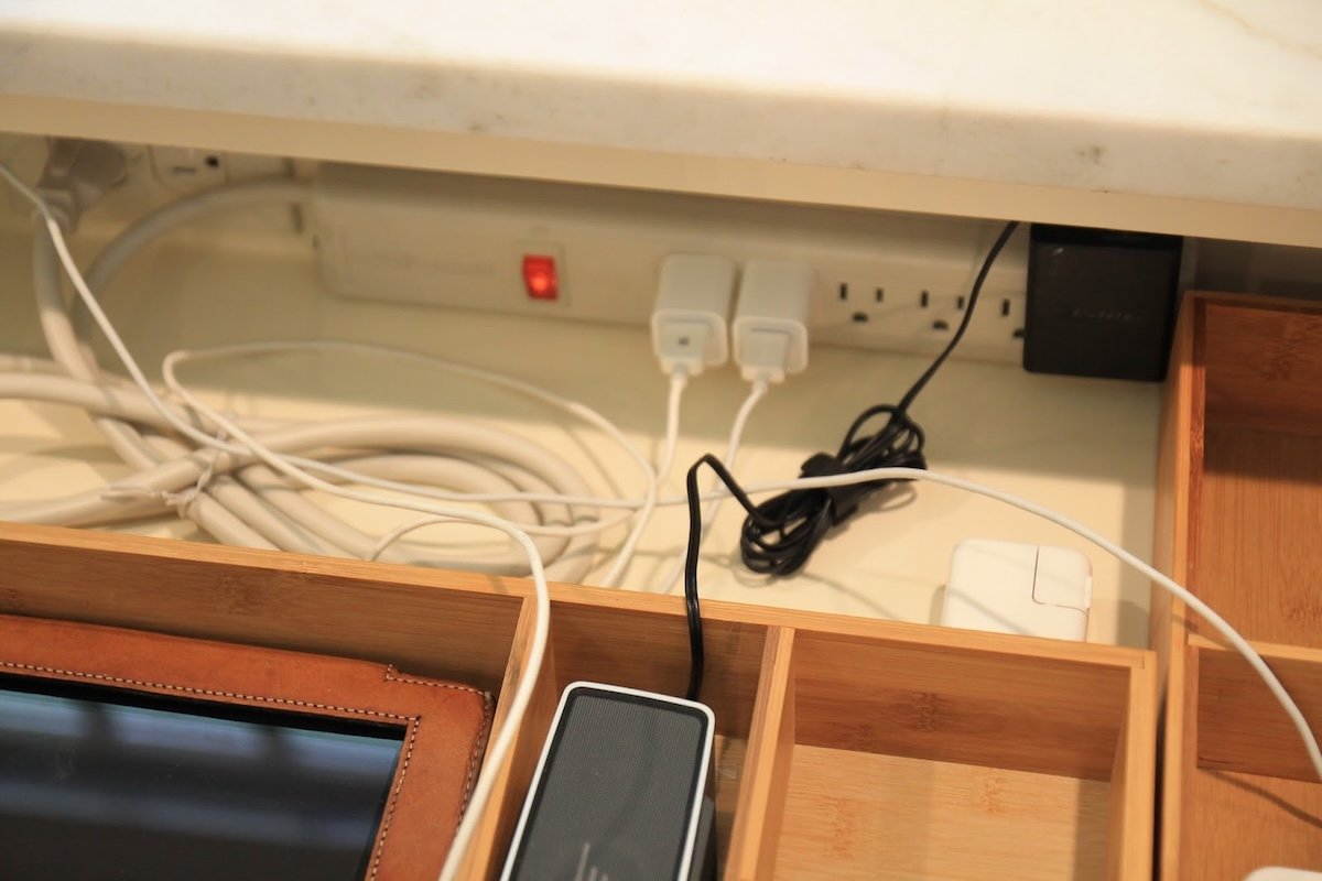 Power strip in the back of a drawer, with phones and devices organized and plugged into the strip.