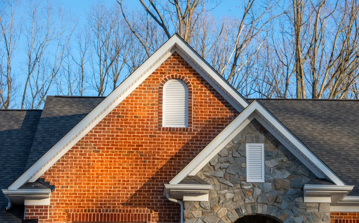 Colonial white round top and vertical gable vents on a brick and stone veneer facade double peak gabled home.