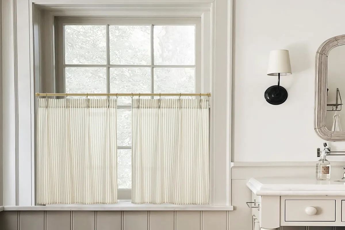 Tan and white apron curtains, which extend a few inches lower than a bathroom window. 