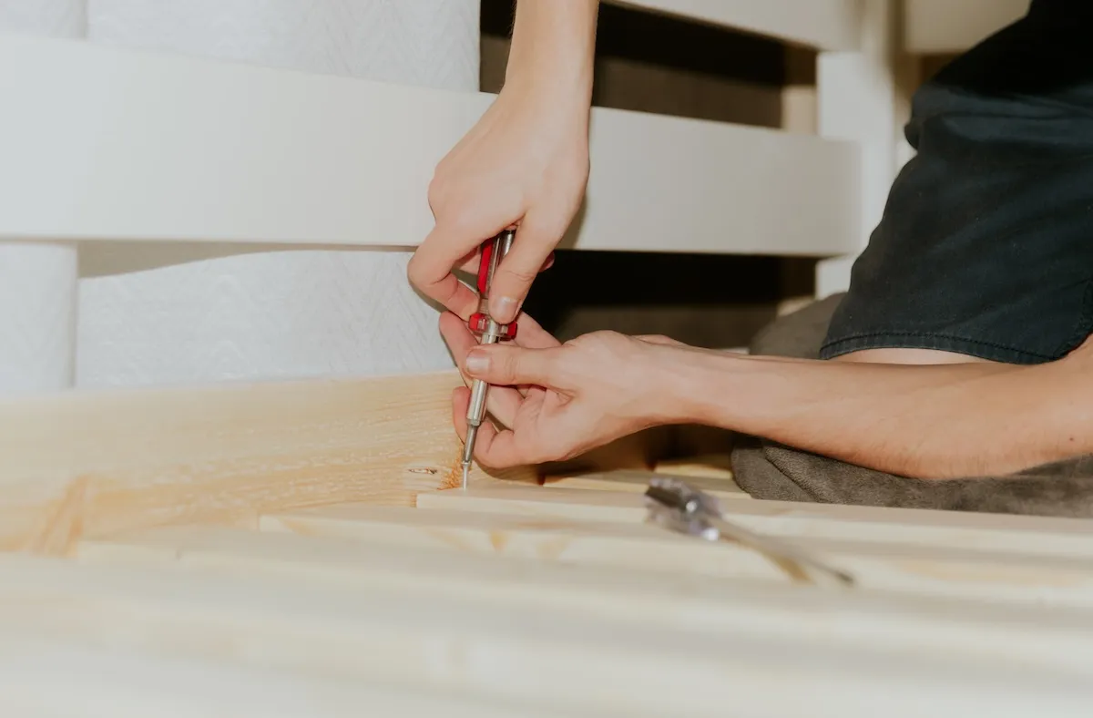 Man sitting sideways on his knees uses a screwdriver to tighten a screw into frame boards on a bunk bed.