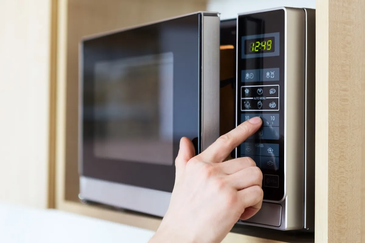 Close up of a male hand pushing a button on a microwave.