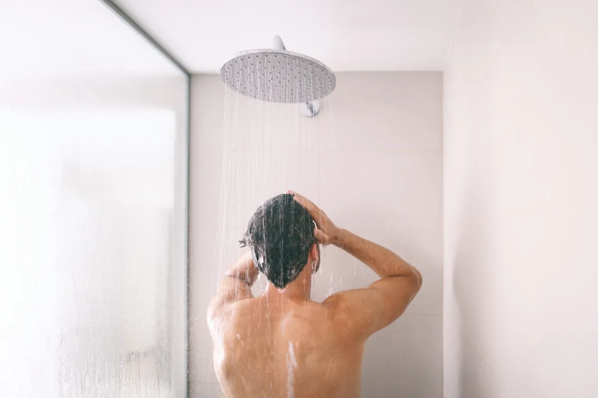 Man taking a shower washing hair with shampoo product under water falling from luxury rain shower head.