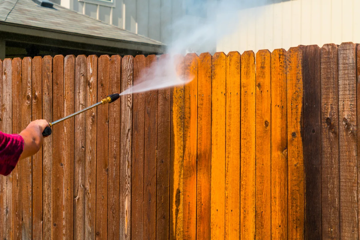 Person pressure washing a wood fence.