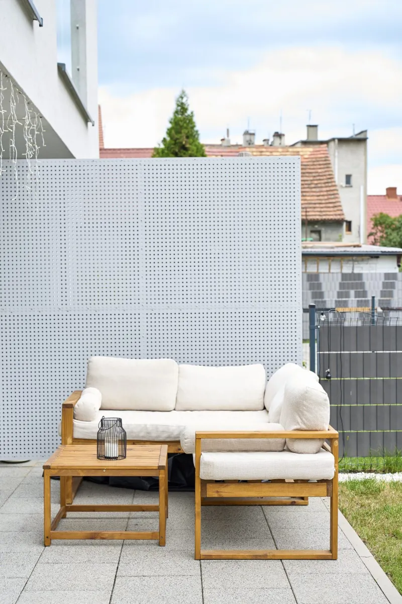 Wooden patio sofa, chair and table arranged beside perforated privacy screen.
