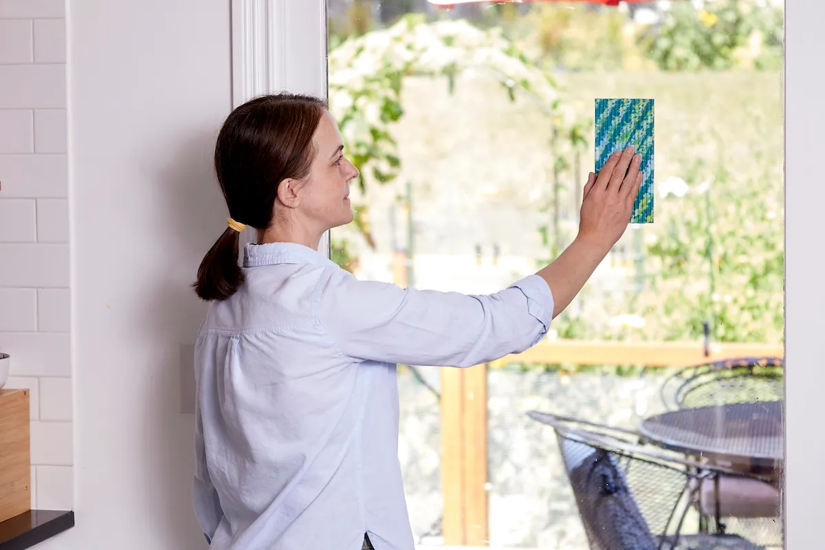 Woman stands by sliding glass door and hangs a piece of fly paper on the glass.
