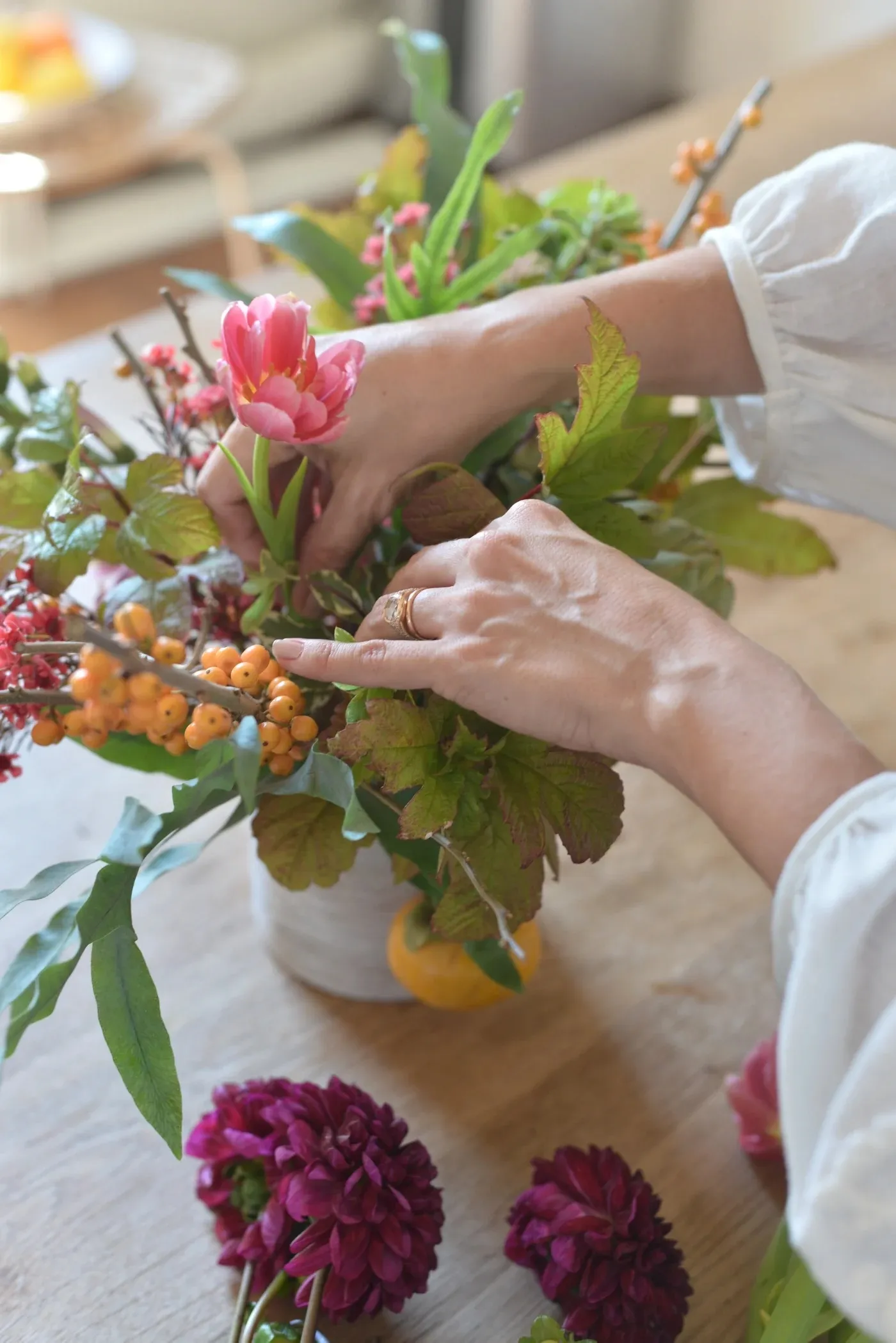 View of woman's hands arranging fall  flowers in a vase.