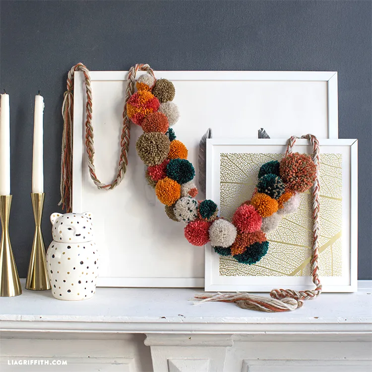 A pom pom garland made in seasonal fall colors, hanging on a white picture frame.