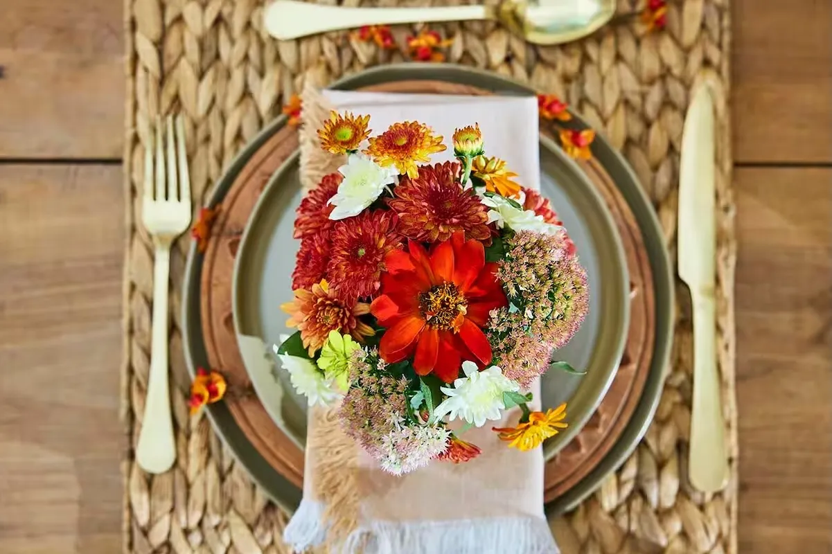 Birds-eye view of fall flowers like mums and zinnias in a bouquet at a formal place setting.