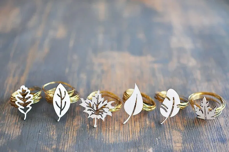 Six golden handmade DIY fall-themed napkin rings laid out on a table.