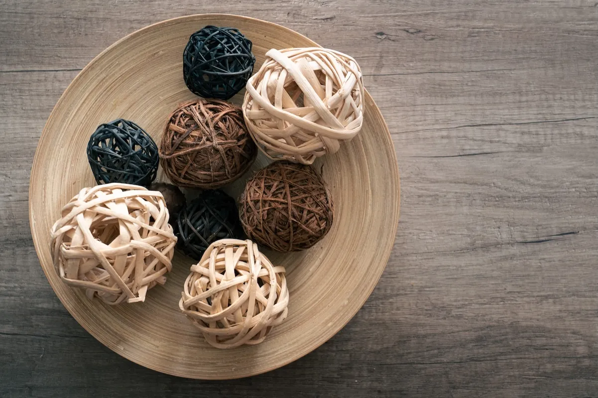 A wood bowl full of natural-colored decorative wicker balls of various sizes.