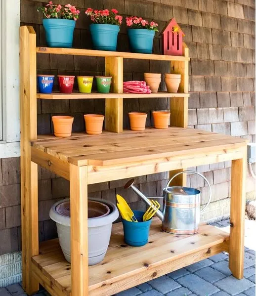 Photo of a cedar potting bench, shelves lined with colorful flower pots, against a wood-shingled house.