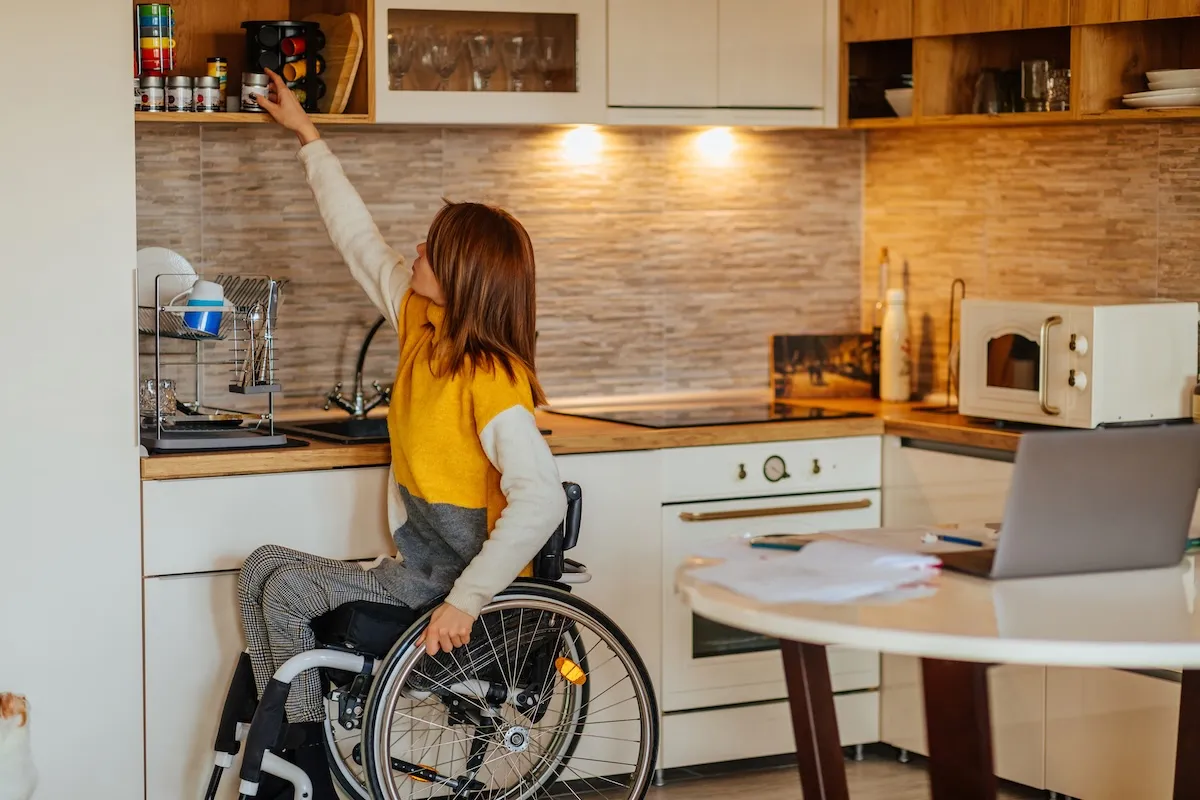 Side view of woman in wheelchair reaching for a jar in the kitchen.