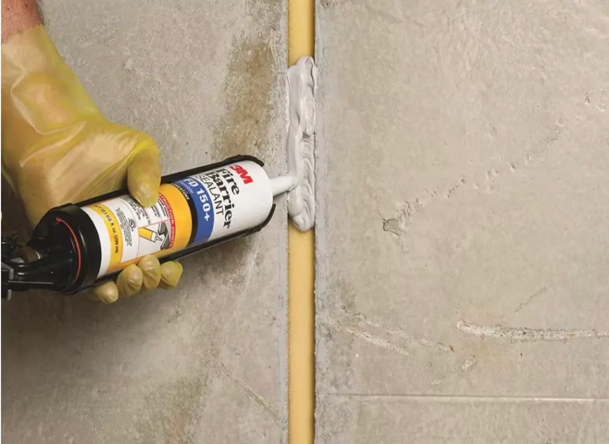 Person applies fire barrier sealant between cracks in walls.