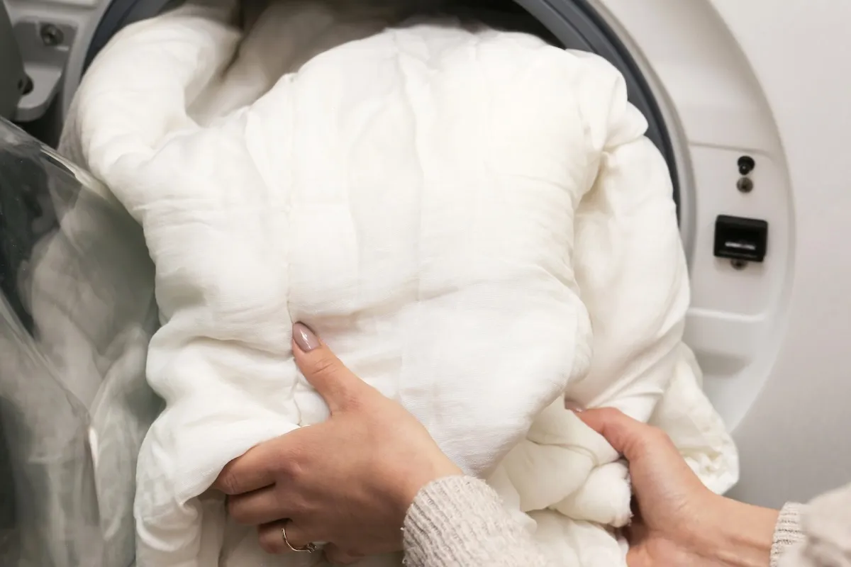 Person shoves a bulky comforter into a front-load washing machine.
