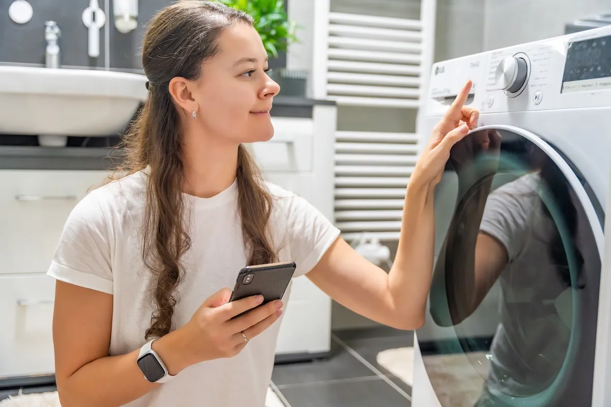 A woman uses her phone to control a smart washing machine. 