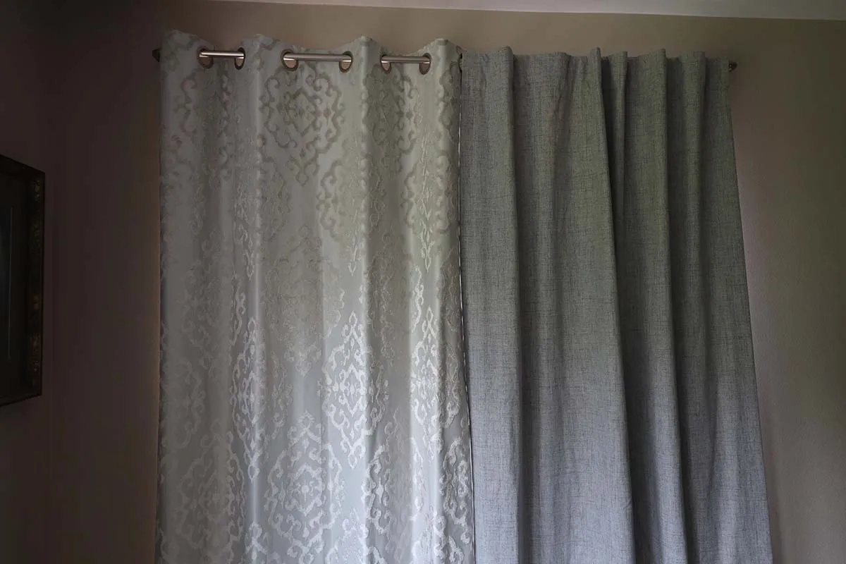 One patterned thermal curtain and one grey thermal curtain installed over a large window.