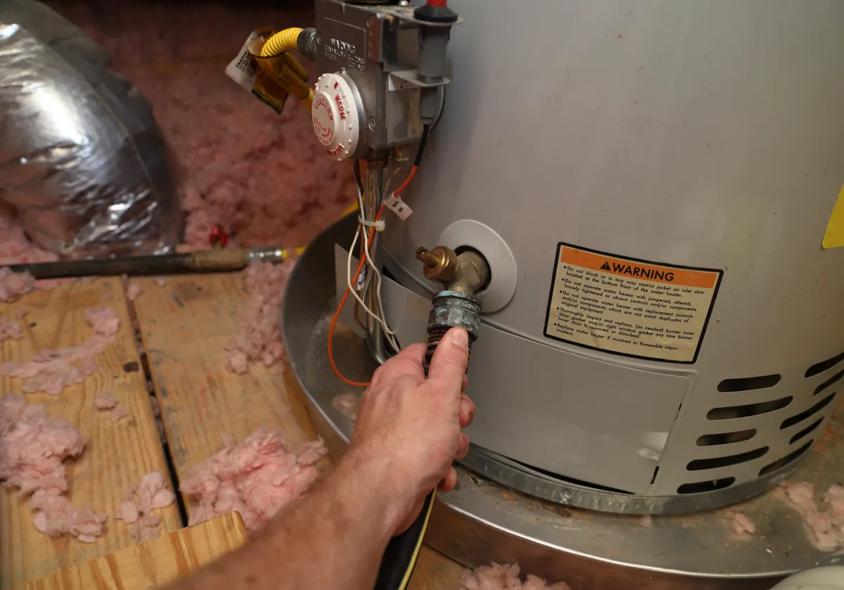 Hand attaches hose to a home water heater to perform maintenance.