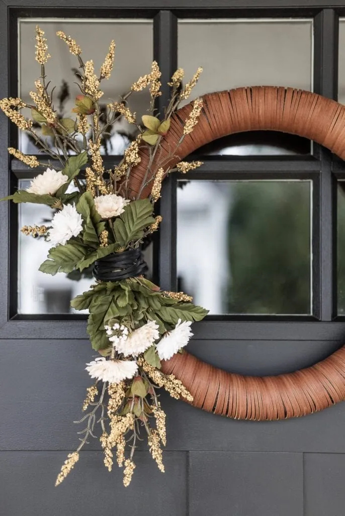 An elegant, smooth leather-wrapped wreath with fall greenery hanging on a front door.
