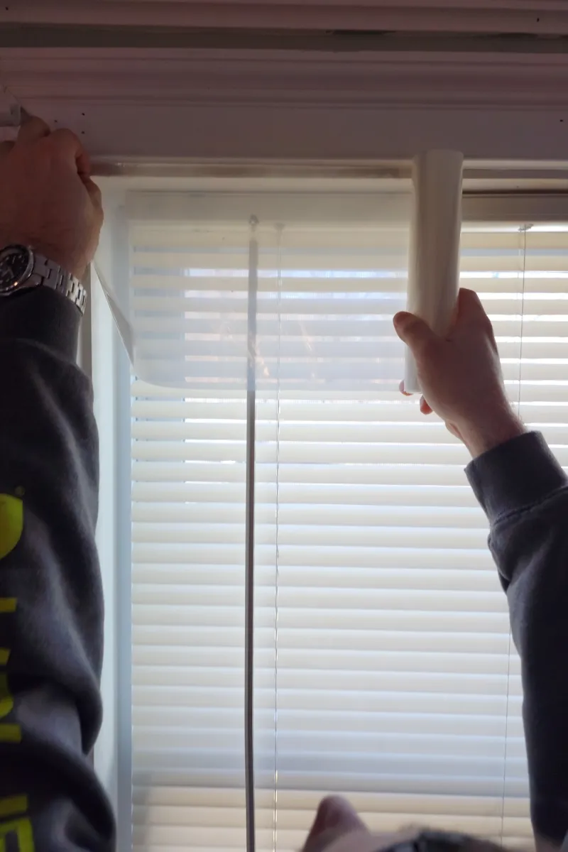 Man unrolls window insulation film in front of a window.