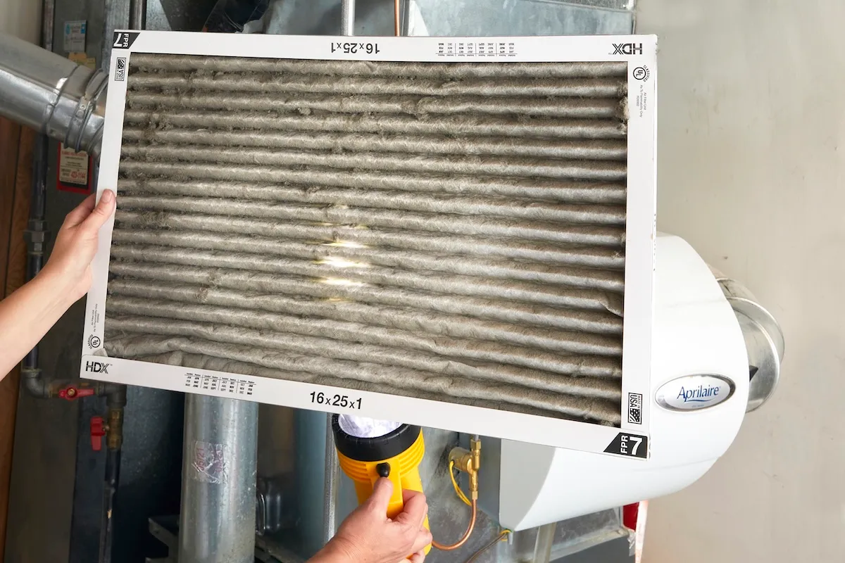 Woman holds a dirty furnace filter and shines a flashlight up from the bottom.
