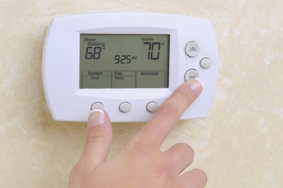 Closeup of a woman's hand setting the room temperature on a programmable thermostat.