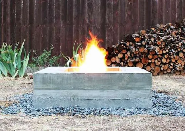 A fire burns inside a rectangular DIY fire pit made of concrete.