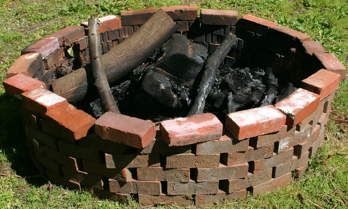 Round DIY fire pit made of red bricks surrounded by grass.