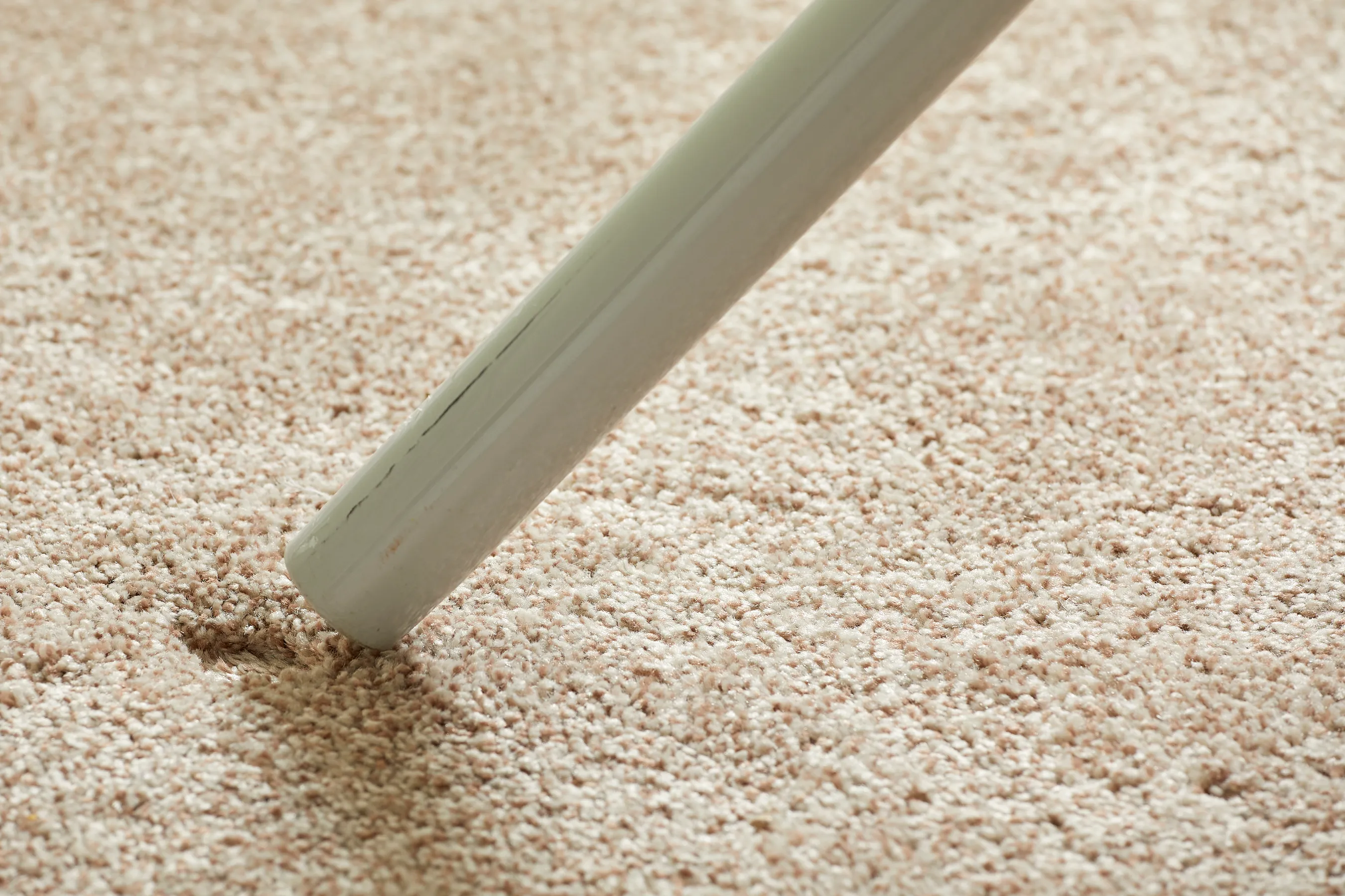 Person uses a vacuum attachment to fluff a carpet dent.