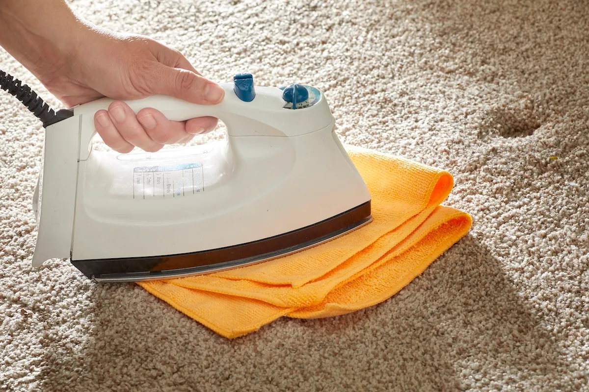Woman irons orange cloth on top of a beige carpet.