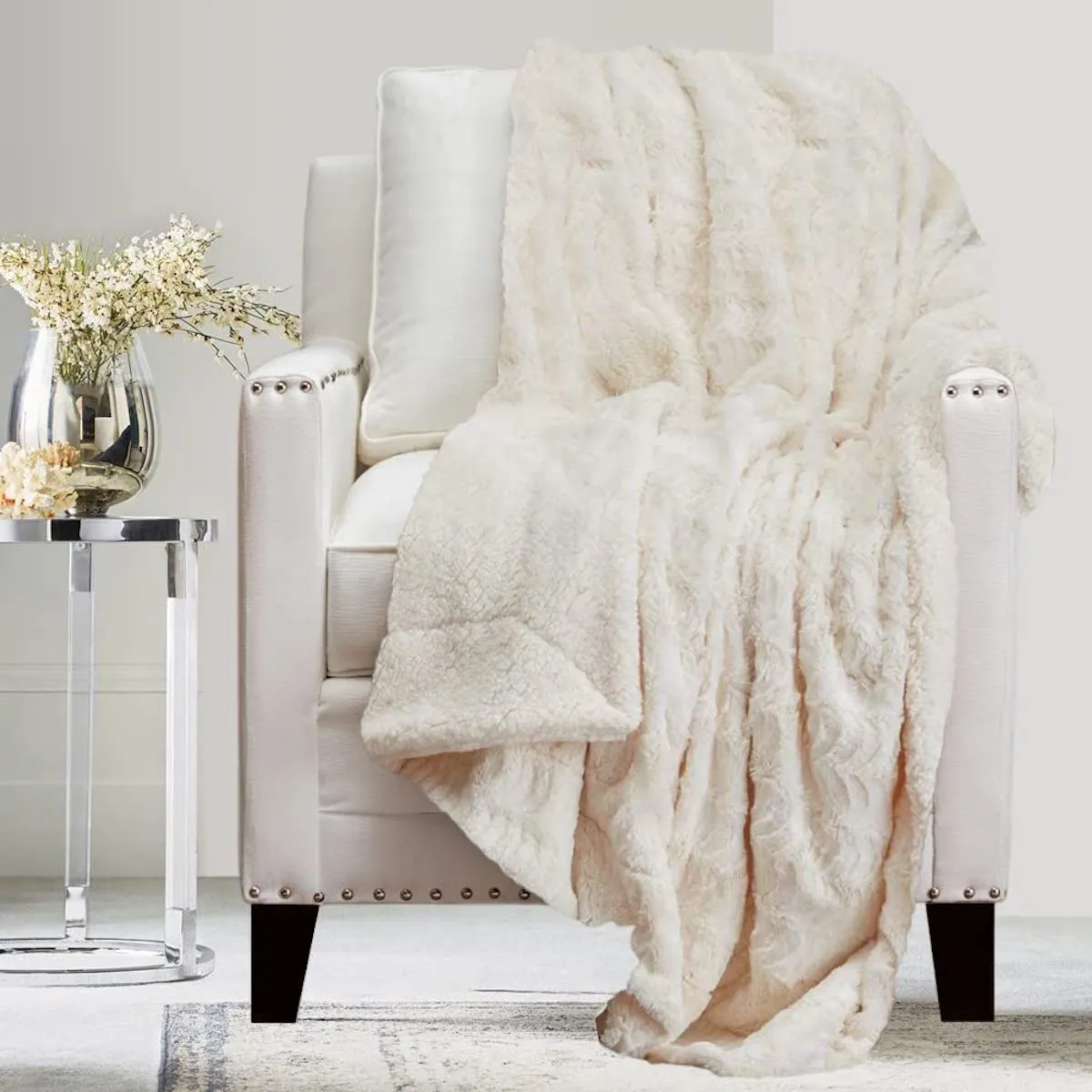 Luxe-looking white living room focusing on a white chair with a fluffy white throw blanket over top.