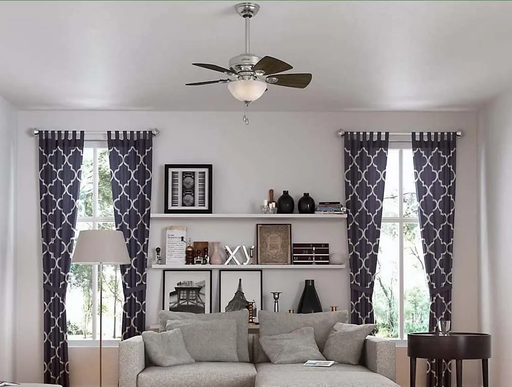View of living area with ceiling fan, light grey couch and grey curtains.
