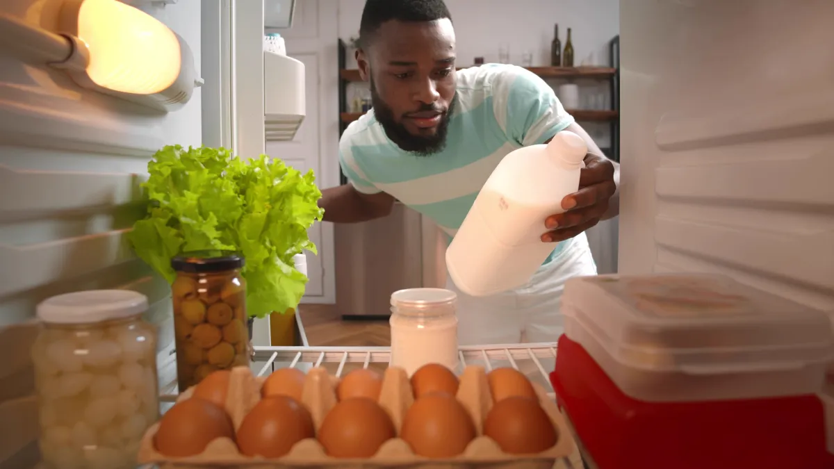 View from fridge of a young man looking inside refrigerator full of food. 